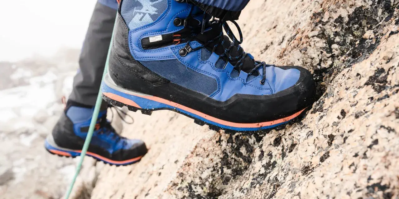 Close-up of a blue and black hiking boot with orange accents, gripping a rocky surface.
