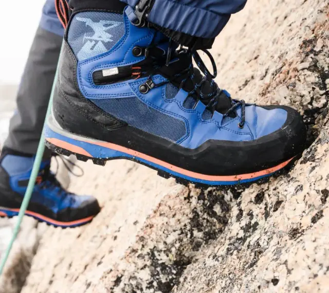 Close-up of a blue and black hiking boot with orange accents, gripping a rocky surface.